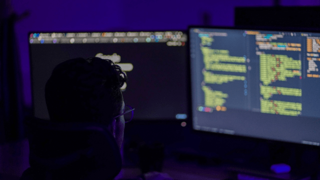 programmer in dark room working on multiple monitors